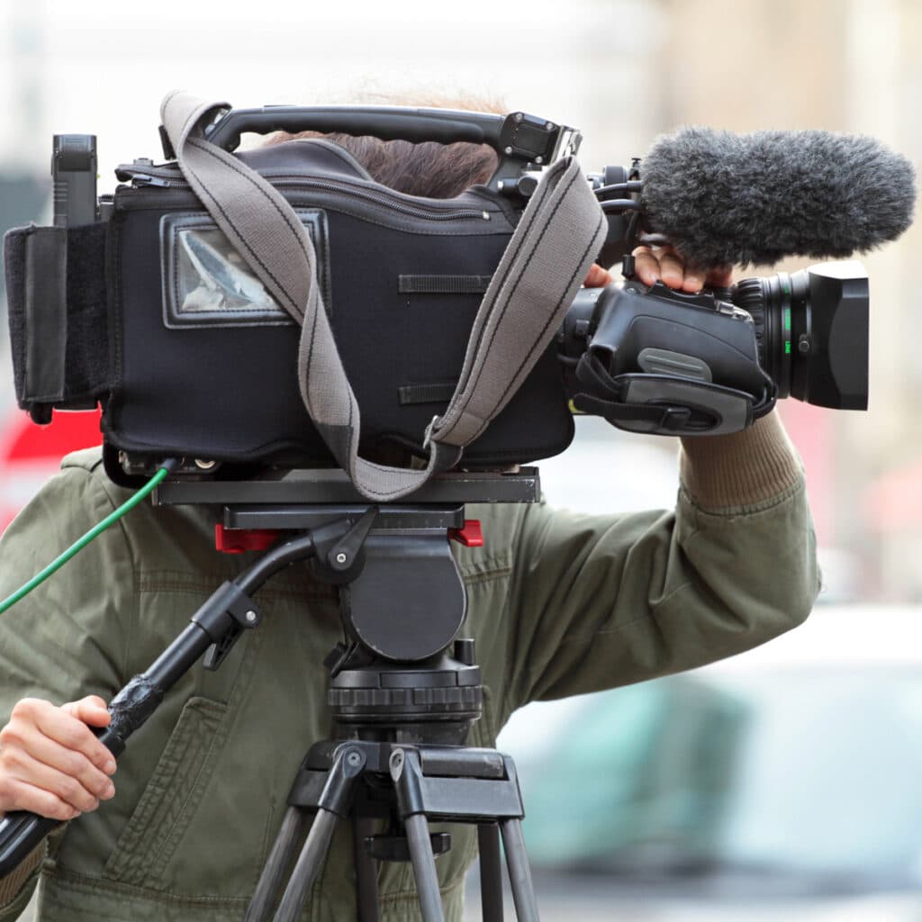 Vidéographe filmant avec caméra vidéo professionnelle équipée d'un microphone sur un tripod robuste.