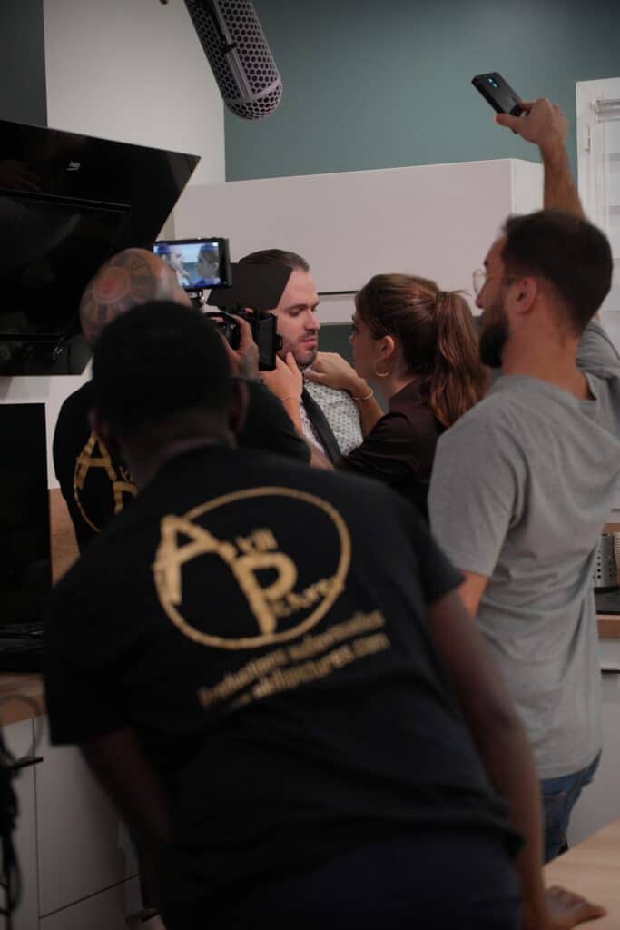Équipe de tournage filmant une scène intense : une femme touche le visage d'un homme. Caméra, micro, et logo AKill Picture visibles.