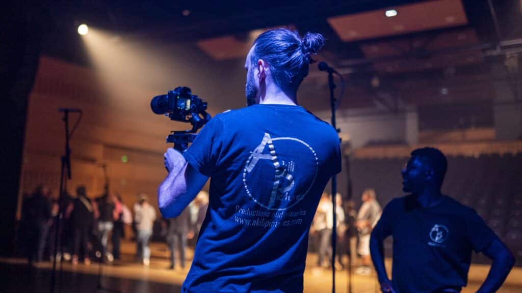 Vidéaste filmant un événement sur scène. T-shirt Akilipictures, Productions audiovisuelles, www.akilipictures.com